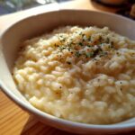 A close-up of a bowl filled with creamy risotto, topped with fresh herbs and black pepper.