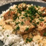 Close-up of creamy smothered chicken and rice, garnished with fresh parsley and paprika.