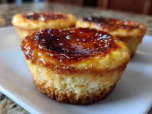 Close-up of a crème brûlée cheesecake cupcake with a caramelized sugar topping on a white plate.