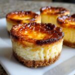 Close-up of four creme brulee cheesecake cupcakes with a golden caramelized sugar topping and graham cracker crust.