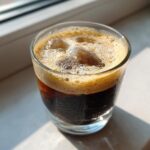 A refreshing glass of New Orleans style creme brulee iced coffee with ice and a frothy top.