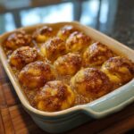 A light blue baking dish filled with golden crescent roll apple dumplings, baked in a syrupy glaze.