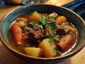A close-up view of a steaming bowl of crock pot beef stew, featuring tender beef chunks, carrots, potatoes, and fresh parsley.