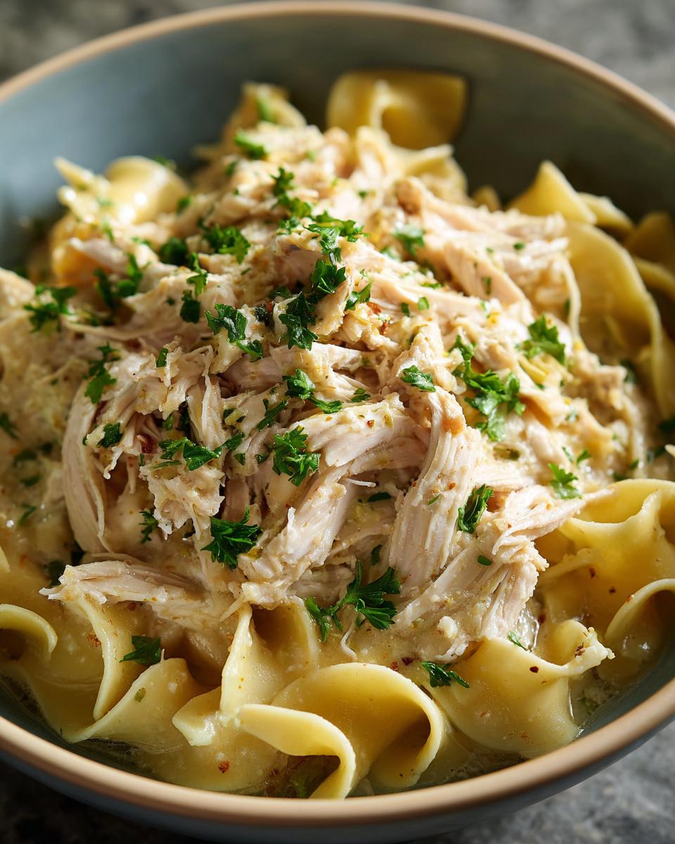 Close-up of a bowl filled with creamy crockpot chicken and noodles, topped with fresh parsley.