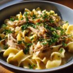 A close-up bowl of homemade crockpot chicken and noodles, topped with fresh parsley.
