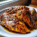 Close-up of tender, seasoned crockpot chicken breasts coated in a rich sauce with visible herbs.