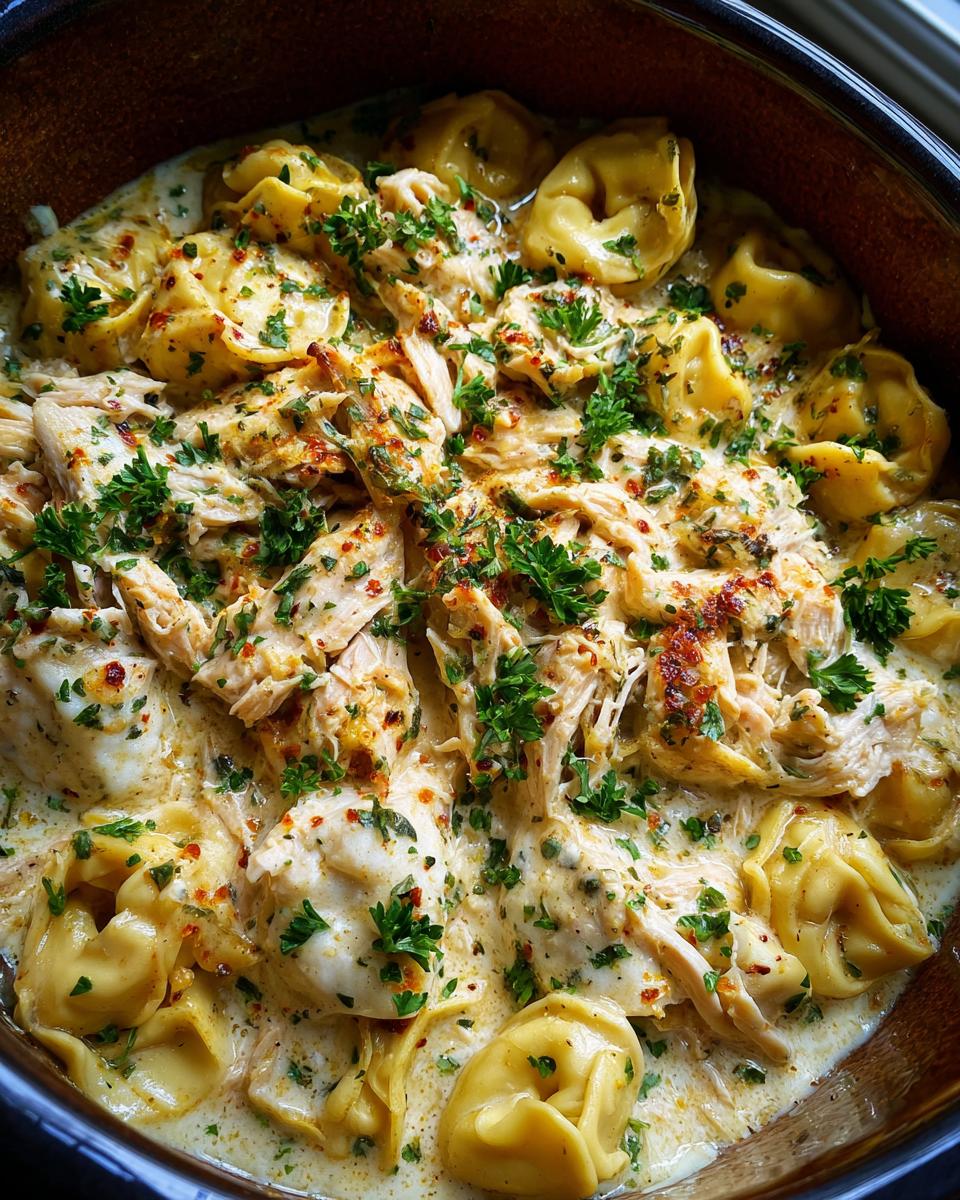 Close-up of creamy Crockpot Chicken Tortellini garnished with fresh parsley and red pepper flakes.