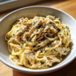 A close-up of a bowl of Crockpot Garlic Parmesan Chicken Pasta, topped with shredded chicken, parmesan cheese, and parsley.