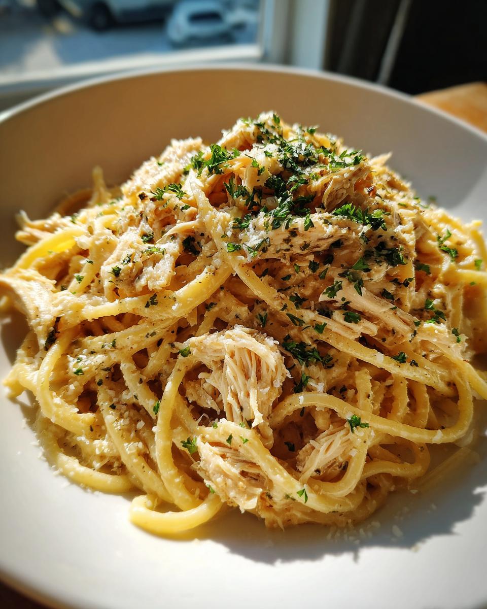 A close-up of Crockpot Garlic Parmesan Chicken Pasta, featuring spaghetti noodles coated in a creamy sauce with shredded chicken and fresh parsley.
