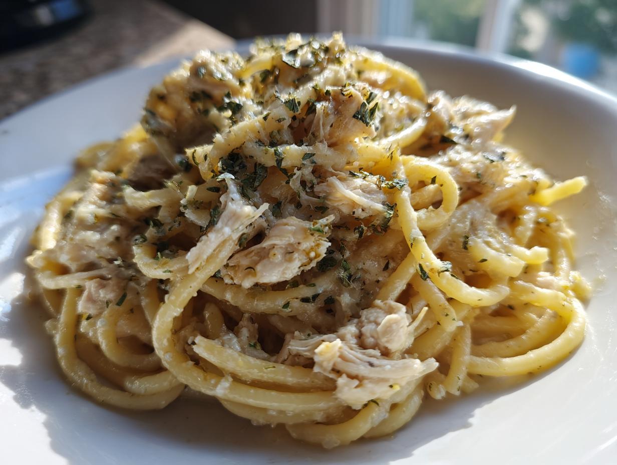 A close-up of Crockpot Garlic Parmesan Chicken Pasta, featuring thick spaghetti noodles coated in a creamy sauce with shredded chicken and herbs.