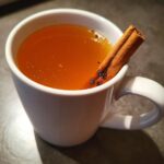 Close-up of a white mug filled with warm Dutch oven apple cider, garnished with a cinnamon stick.