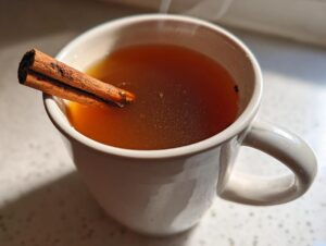 A close-up of a steaming mug of warm Dutch oven apple cider, garnished with a cinnamon stick.
