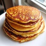 A tall stack of golden brown, fluffy almond flour pancakes on a white plate.