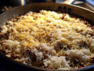 Close-up of French onion beef over rice casserole in a pan, topped with melted shredded cheese.