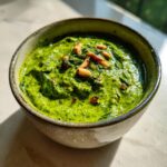 Close-up of vibrant green basil pesto in a rustic bowl, topped with pine nuts and chili flakes.