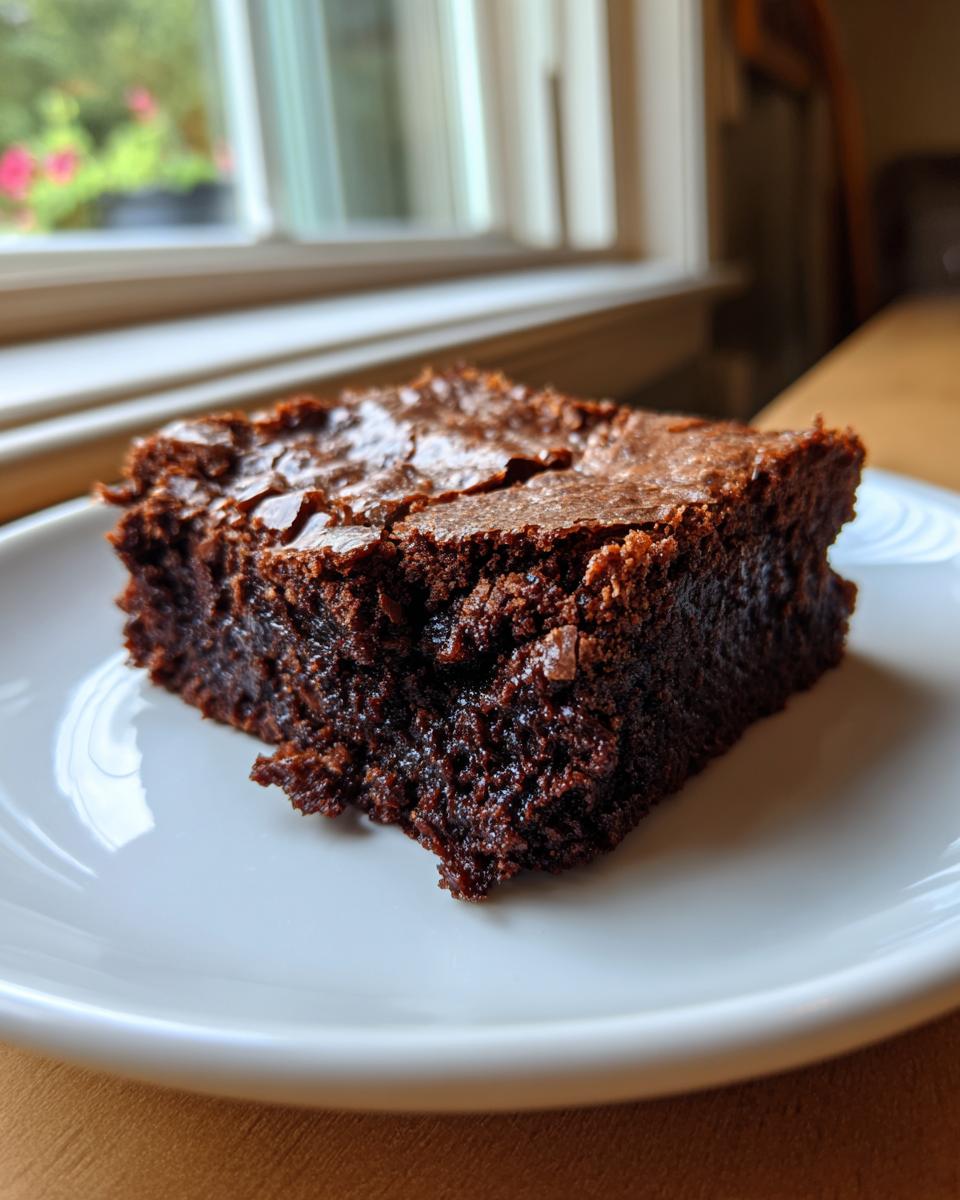 A close-up of a fudgy sourdough discard brownie on a white plate, with a cracked top.