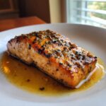 A perfectly cooked fillet of garlic butter salmon glistening in its sauce on a white plate.