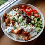 A delicious bowl of Greek chicken tzatziki, featuring rice, grilled chicken, cucumber, tomato, olives, feta, and tzatziki sauce.