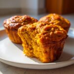 Close-up of a moist Greek yogurt pumpkin muffin with a bite taken out, showing its fluffy texture.