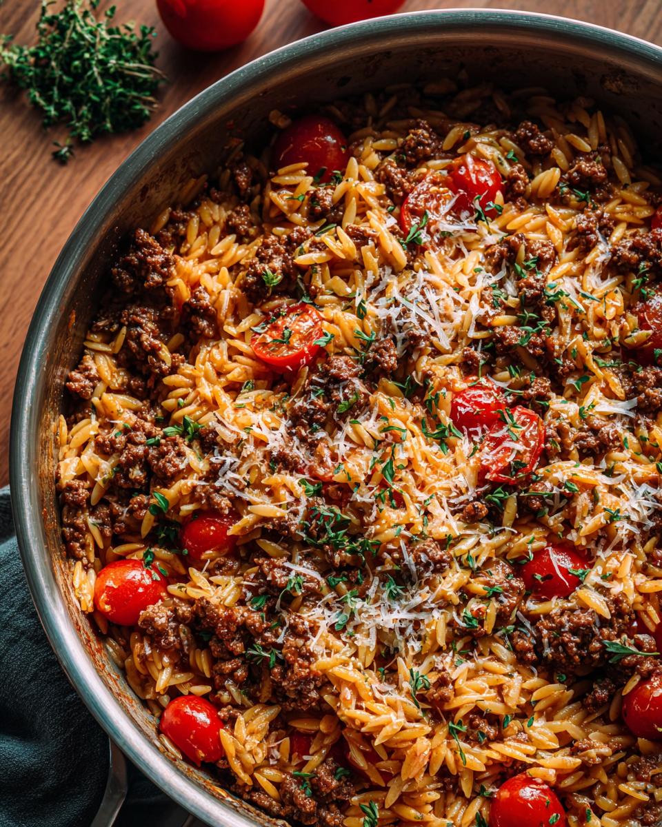 Close-up of a skillet filled with ground beef orzo, cherry tomatoes, and grated cheese.