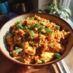 A close-up shot of a bowl filled with delicious ground chicken fried rice, garnished with chopped green onions.