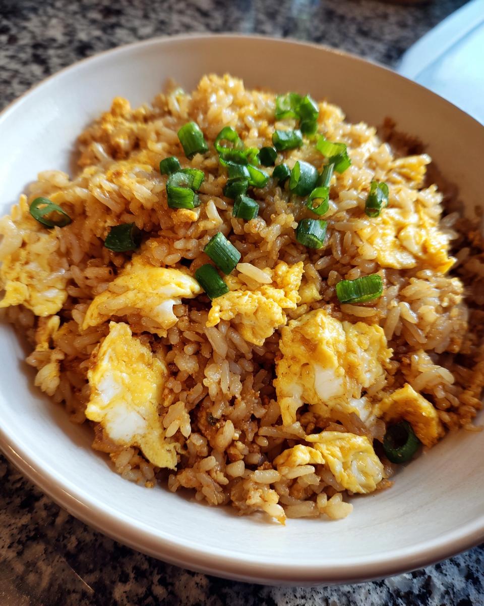 A bowl of delicious ground chicken fried rice with scrambled egg pieces and green onions.