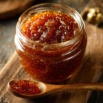 A close-up of a jar filled with rich, dark homemade apple butter, with a spoonful of apple butter in the foreground.