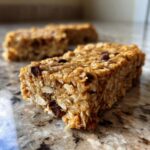 Close-up of homemade protein bars with oats and chocolate chips on a speckled countertop.