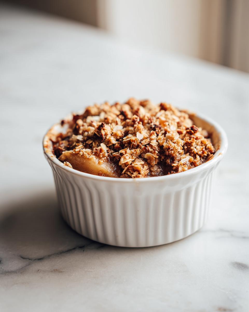 Close-up of a single-serving apple crisp in a white ramekin, topped with a golden-brown crumble.