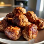 A close-up, stacked pile of ultra-tender Italian meatballs on a white plate, glistening under warm light.