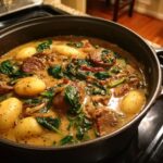 A close-up of a pot filled with Italian sausage gnocchi soup, featuring tender gnocchi, sliced Italian sausage, and wilted spinach in a creamy broth.