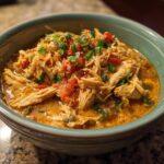 A close-up of a bowl of Keto cream cheese chicken chili, topped with diced tomatoes and green onions.