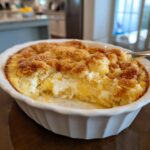 A close-up of a freshly baked lemon cream cheese dump cake in a white baking dish, with a scoop removed.