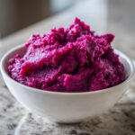 A close-up of vibrant mashed purple sweet potatoes served in a white bowl.
