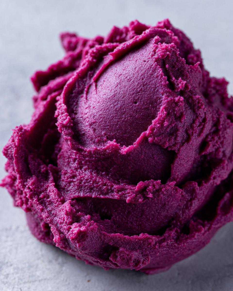 A close-up, macro shot of a scoop of vibrant mashed purple sweet potatoes with a creamy texture.