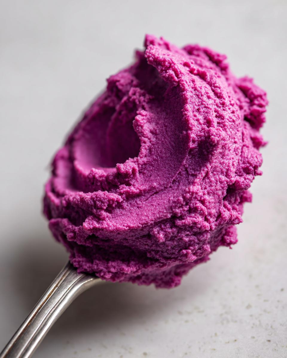 A close-up shot of a spoonful of vibrant mashed purple sweet potatoes, showcasing its creamy texture.