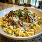 A hearty bowl of old fashioned beef stroganoff served over egg noodles, topped with mushrooms and fresh parsley.