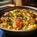 Close-up of golden brown chicken pieces nestled in creamy pasta, garnished with fresh parsley, in a one-pan chicken and noodles dish.