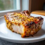 A close-up of a perfectly cooked oven baked pork chop on a white plate, showing its juicy interior and seasoned crust.
