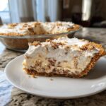 A slice of no-bake Pecan Cream Pie on a white plate, showing layers of creamy filling and crunchy crust, topped with whipped cream and pecans.
