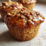 Close-up of a moist pecan pie muffin topped with a glossy glaze and chopped pecans.