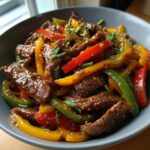 A close-up of a bowl filled with vibrant pepper steak, featuring tender strips of beef and colorful bell peppers.