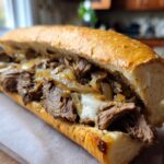 Close-up of a homemade Philly Cheesesteak sandwich overflowing with thinly sliced steak, melted cheese, and caramelized onions on a toasted roll.