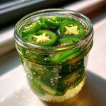 Close-up of a glass jar filled with vibrant green pickled jalapeños submerged in brine.