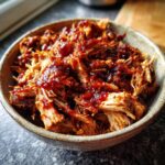 Close-up of a bowl filled with juicy, tender pulled pork covered in barbecue sauce.