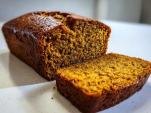 A close-up of a moist pumpkin banana bread loaf with one slice cut, showcasing its rich texture.