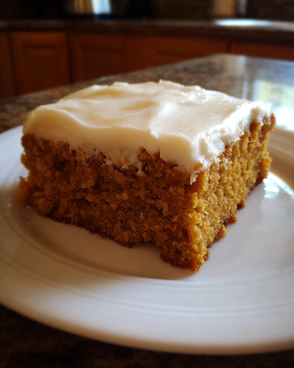 A close-up of a delicious pumpkin bar with thick, creamy frosting on a white plate.
