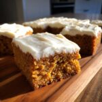 Close-up of a slice of pumpkin bars with creamy frosting on a wooden board.
