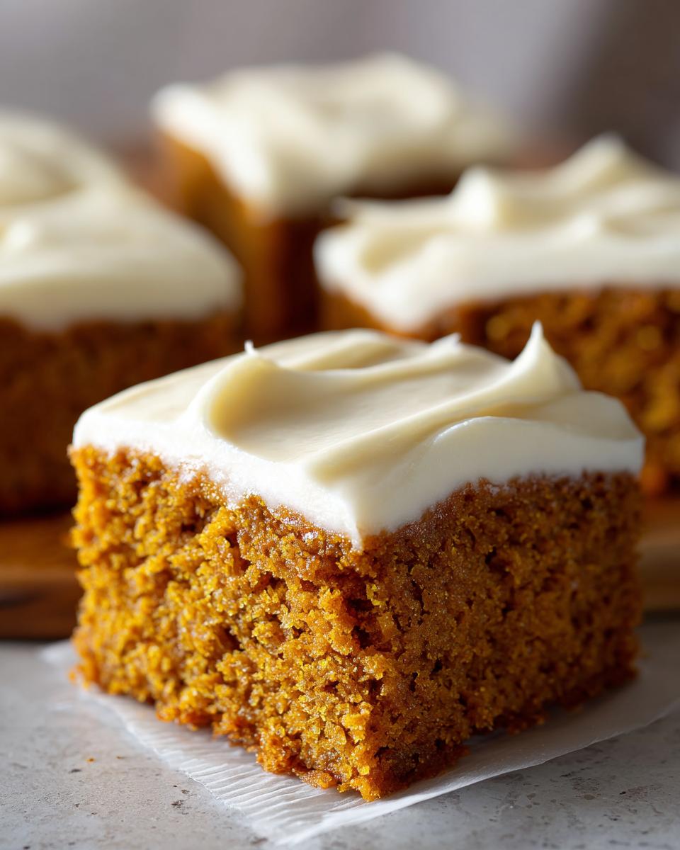 A close-up of a moist pumpkin bar topped with thick, creamy frosting.