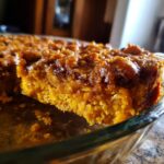 A close-up of a slice of pumpkin oatmeal dump cake in a glass baking dish, showing its moist texture and crumbly topping.